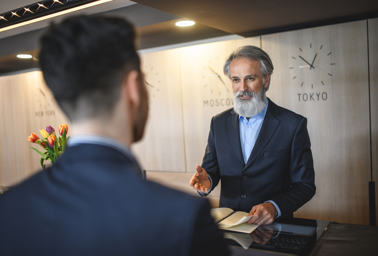 Courteous Senior Hotel Receptionist Assisting Businessman